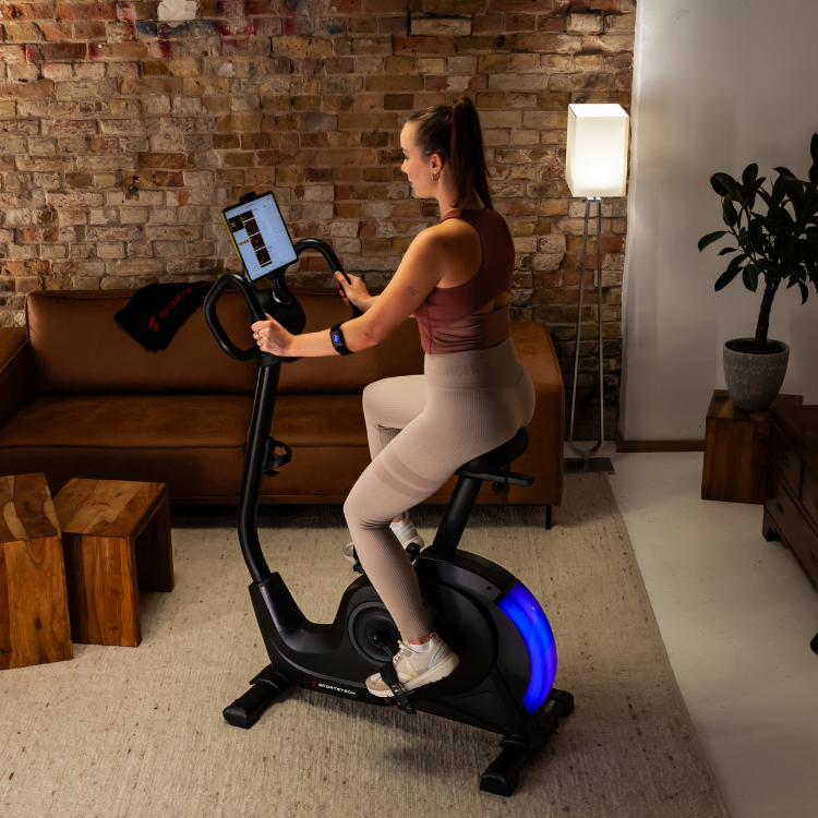 Frau beim Indoor-Training auf einem Ergometer vor Backsteinwand