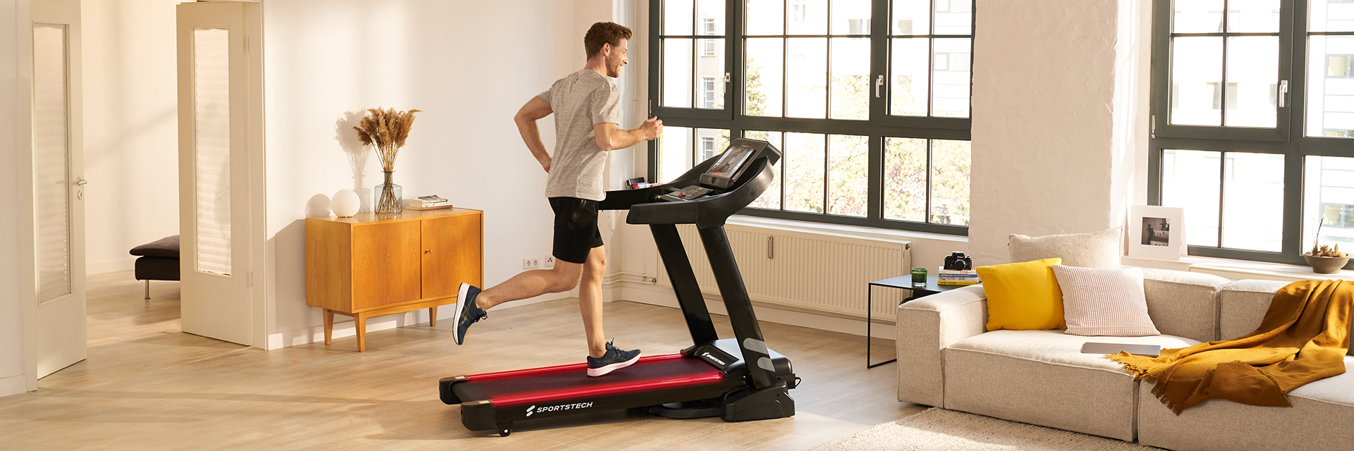 Tapis de course noir F10 Sportstech Femme en tenue de sport courant sur le tapis de course noir F10 dans le salon